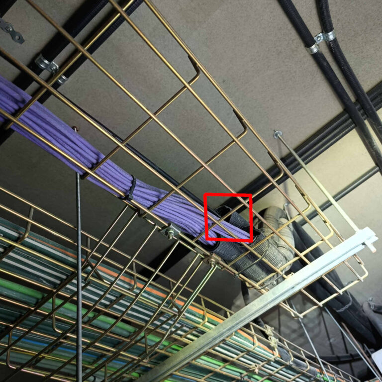 Detalle de la entrada del cable de fibra óptica desde la rejilla aérea a un tubo corrugado vertical para su subida a la planta superior