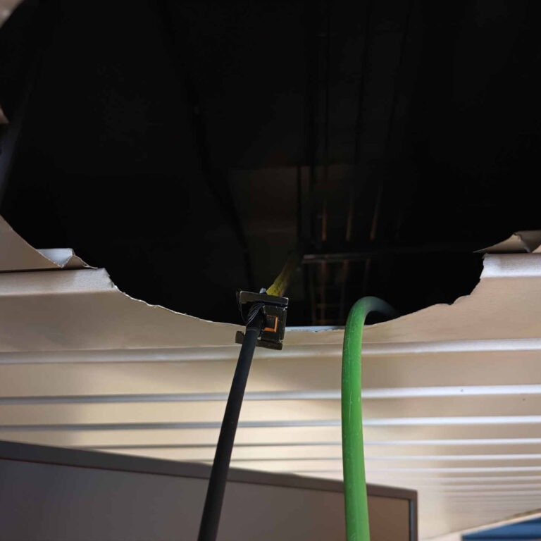 Detalle de un orificio de foco en techo de aluminio con canto vivo, donde la fibra óptica se guía atada a un metro para evitar rozaduras y daños durante el tendido