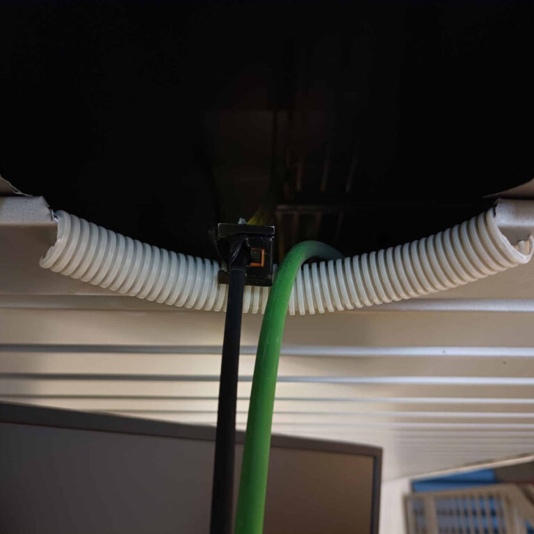 Protección del canto vivo del orificio en techo de aluminio mediante un tramo de tubo corrugado recortado, evitando rozaduras y daños en la fibra óptica