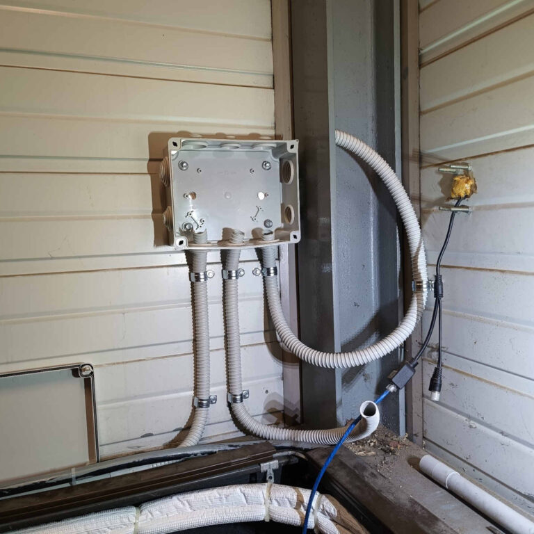 Caja de derivación instalada en estructura metálica con tubos corrugados para cableado de videovigilancia en nave industrial