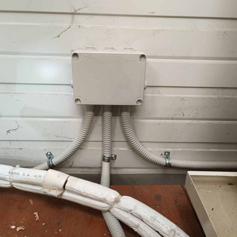 Caja de derivación instalada en pared de nave industrial con tubos corrugados para cableado de cámaras de videovigilancia