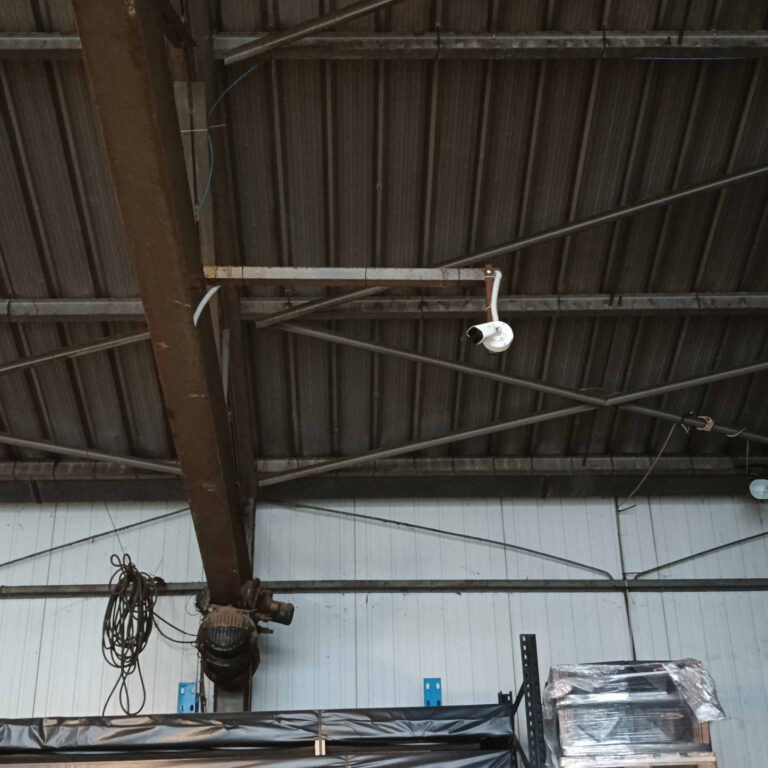 Cámara de videovigilancia instalada sobre poste metálico en el interior de una nave industrial para control de zonas elevadas