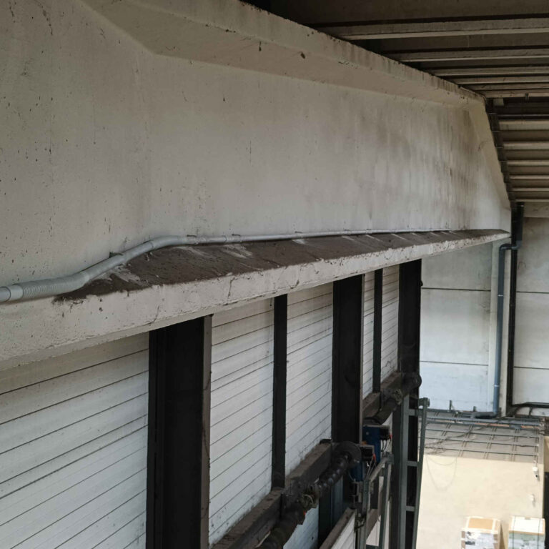 Canalización de cableado mediante tubo rígido y curvas flexibles instalada sobre viga horizontal en el techo de una nave logística