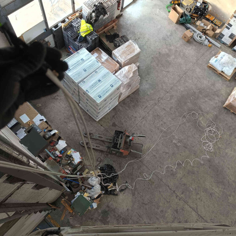 Vista desde la cesta de una plataforma elevadora durante el paso de cable de red mediante guía por el tubo rígido instalado en nave logística