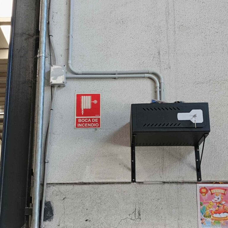 Armario de seguridad instalado en nave industrial con entrada de cableado por tubos independientes para corriente y datos, y caja de derivación cerrada