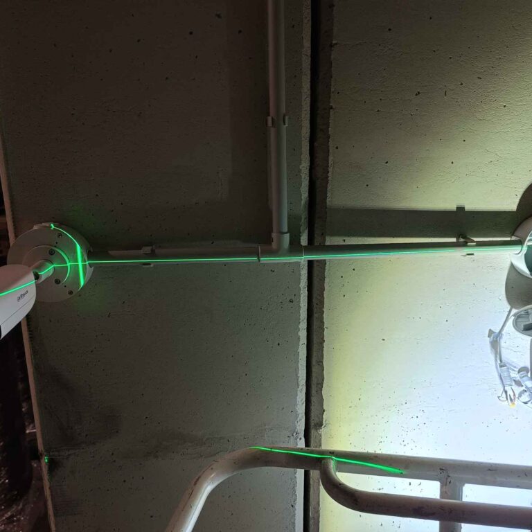 Instalación de tubo horizontal y cajas herméticas Dahua alineadas mediante láser, realizada con apoyo de linterna debido a la escasa iluminación en la nave