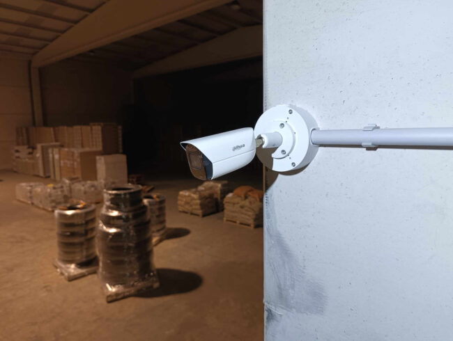 Cámara de videovigilancia Dahua instalada sobre pilar interior de nave industrial, mostrando el entorno monitorizado en condiciones de escasa iluminación