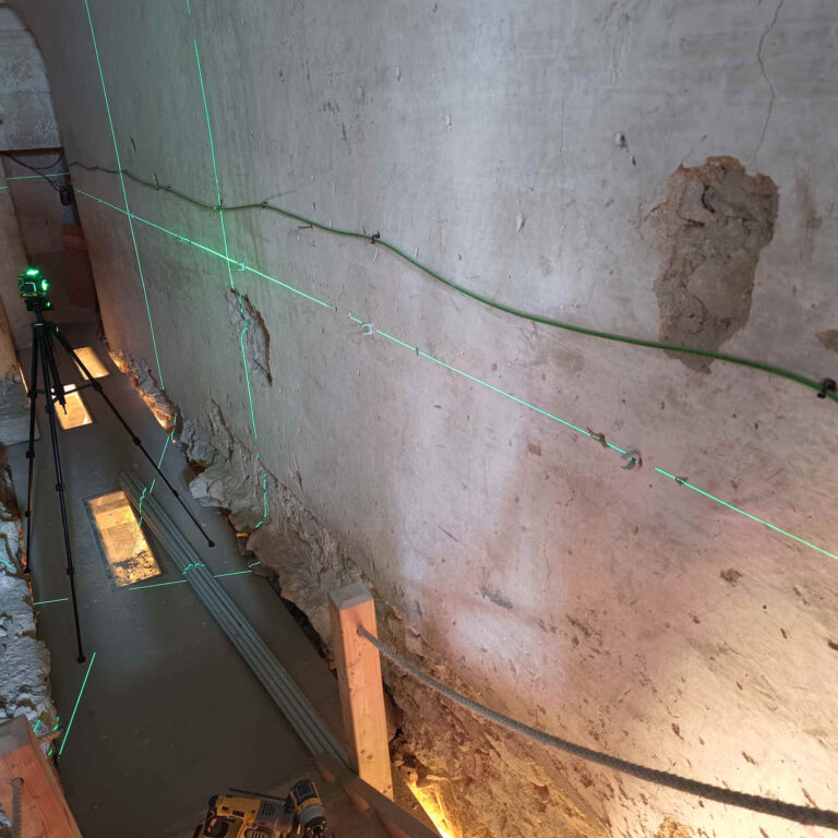 Instalación de tubo PVC para cableado con nivel láser en pared de piedra en espacio reducido