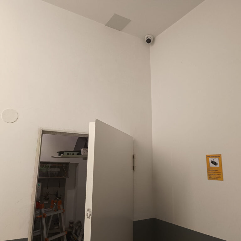 Cámara domo de videovigilancia instalada en una zona de paso del portal junto a cartelería informativa de videovigilancia