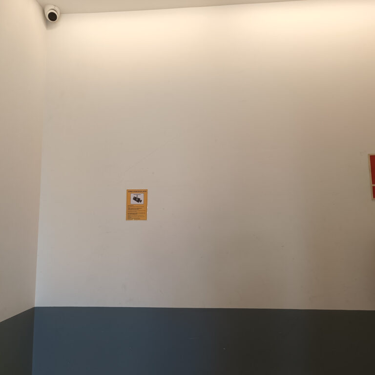 Cámara de seguridad instalada en una zona común del portal junto a señalización disuasoria de videovigilancia y extintor comunitario.