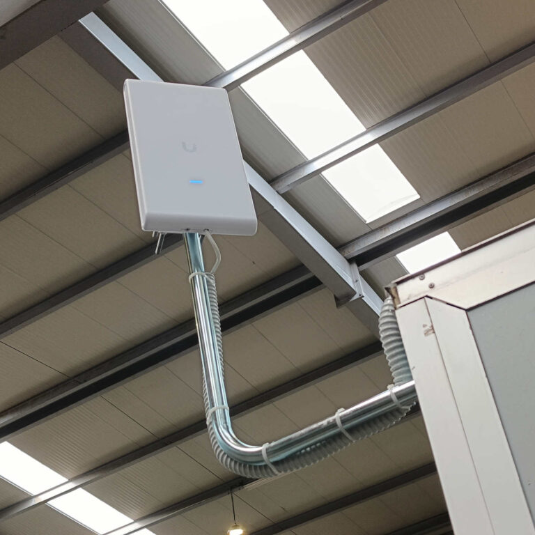 Instalación finalizada del punto de acceso Wi-Fi UniFi U6 Mesh Pro con cableado protegido en nave industrial de acero
