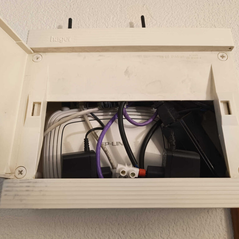 Antiguo punto de acceso WiFi instalado en una caja de comunicaciones con espacio reducido y cableado acumulado antes de la renovación de la red inalámbrica