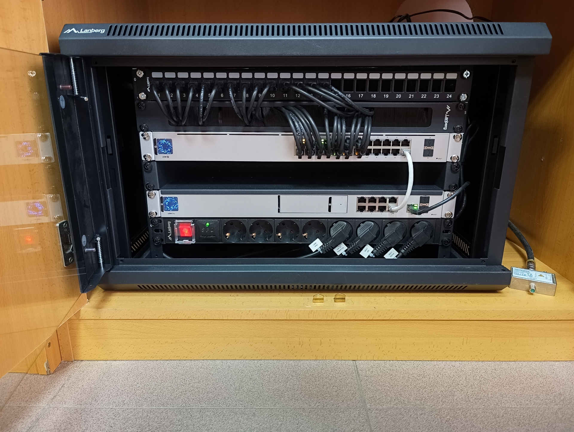 Nuevo armario rack con la infraestructura de red profesional instalada Armario rack con gateway Ubiquiti UniFi Dream Machine Pro, switch PoE de 24 puertos y patch panel tras la renovación de la infraestructura de red de una residencia de estudiantes