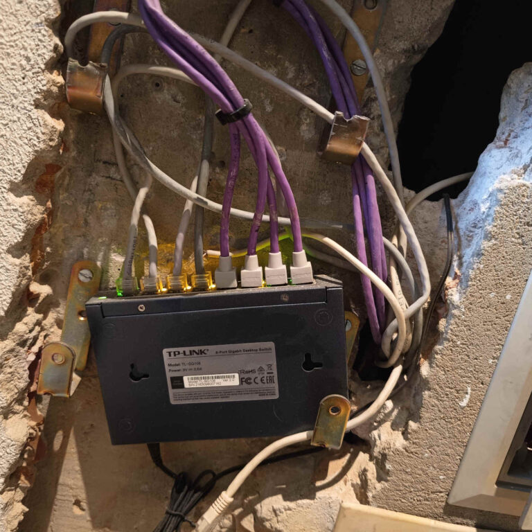 Nuevo switch de distribución Ubiquiti UniFi instalado en el hueco existente de la pared, con el cableado reorganizado y los enlaces principales correctamente identificados mediante etiquetas.