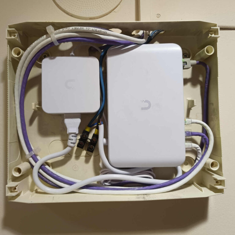 Interior de la caja de superficie donde se aloja la electrónica de distribución de la red WiFi, con switch Ubiquiti UniFi, fuente de alimentación y cableado correctamente organizado