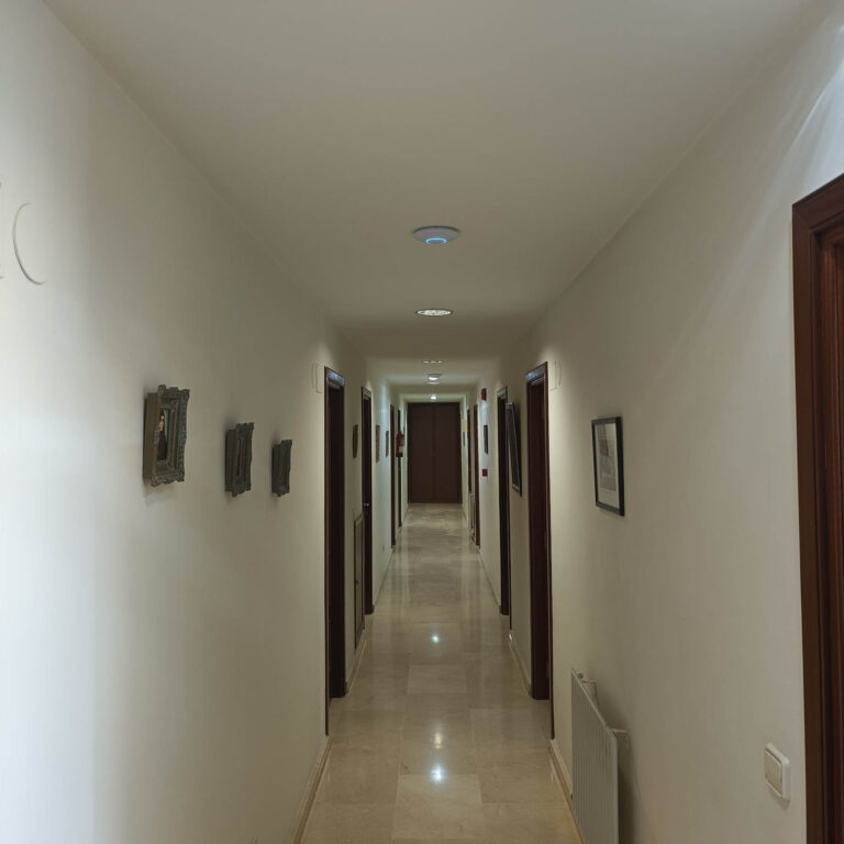 Pasillo de la residencia de estudiantes con varios puntos de acceso WiFi Ubiquiti UniFi instalados estratégicamente para proporcionar una cobertura inalámbrica uniforme en todas las habitaciones